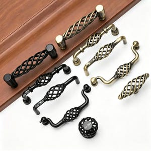 Puede incluir: Una colección de tiradores de armario y un pomo con un diseño de metal trenzado en forma de jaula. Los herrajes están disponibles en acabados negro mate y latón antiguo. Algunas piezas llevan el texto Evan Matik impreso en el metal.