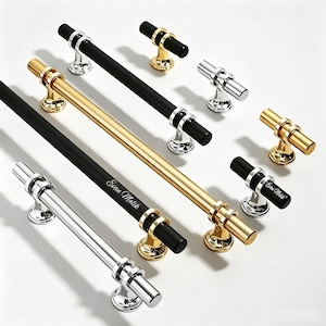 May include: A collection of cabinet hardware including long bar pulls and T-shaped knobs in polished chrome, brushed gold, and matte black finishes. Some pieces feature the engraved text Evan Malik on the bar surface with circular mounts.