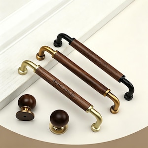 May include: Two long cabinet pulls with wood-grain cylinders and metallic ends, one with gold-tone hardware and one with black hardware. A third pull features gold-tone hardware and the text EVAN MALIK. Two round wooden knobs with metallic bases.