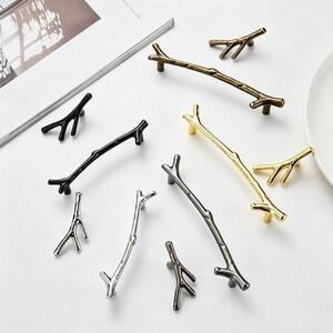May include: A collection of cabinet hardware shaped like tree branches, including long pulls and small knobs. The set features various metallic finishes such as antique bronze, polished gold, matte black, silver, and dark gray, all with textured surfaces.
