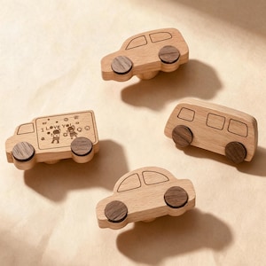 May include: Four wooden drawer knobs shaped like vehicles. Three knobs are cars or vans with dark wood wheels and engraved window outlines. One knob is a truck featuring an engraved illustration of two children and the text I LOVE YOU.
