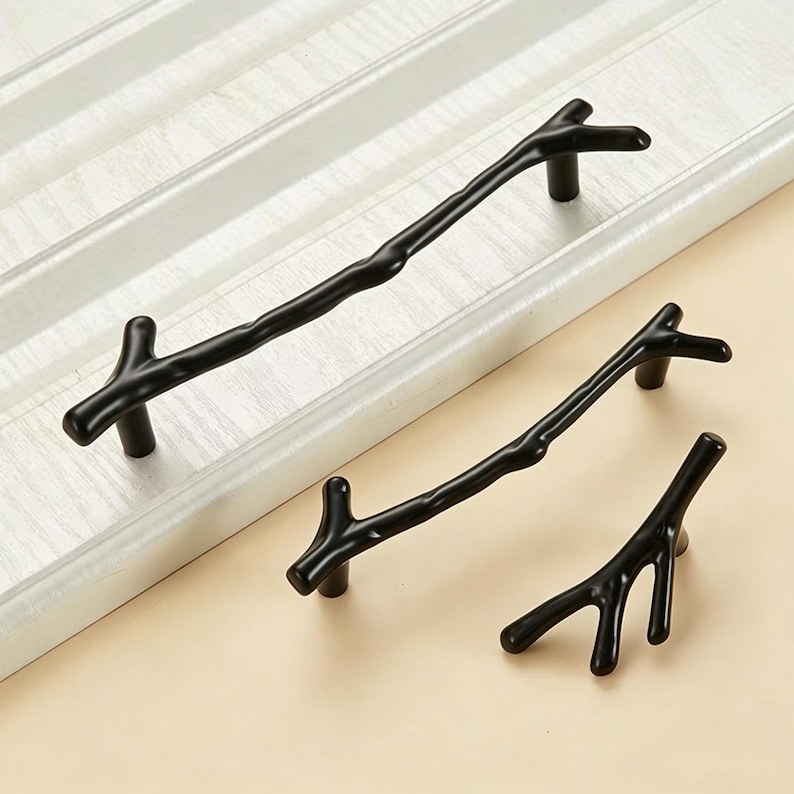 May include: Three matte black cabinet pulls shaped like tree branches. The set includes one long handle, one medium handle, and one smaller knob, each featuring a textured, organic form with small offshoot twigs extending from the main body.