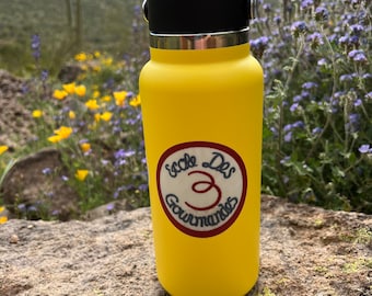 May include: Yellow water bottle with a black lid and a round sticker that says "Ecole Des Gourmandes 3" in French.