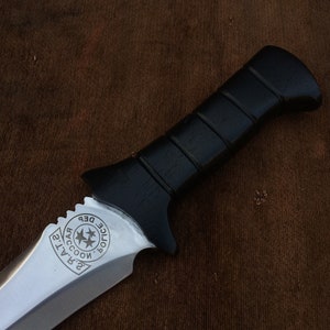 May include: A black-handled knife with a silver blade. The blade has a serrated edge and a circular design with the text "Raccoon City Police Dept." engraved on it.