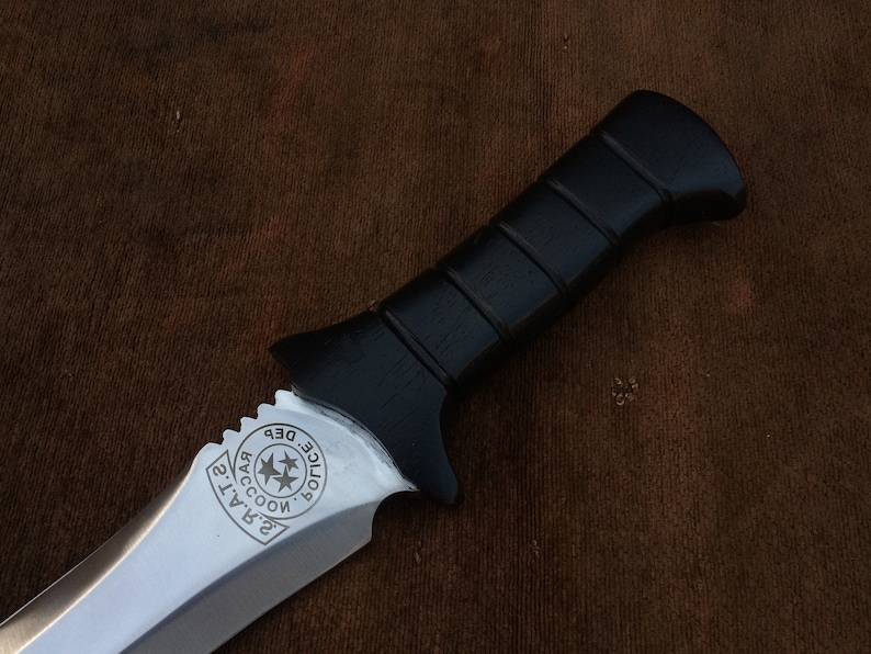 May include: A black-handled knife with a silver blade. The blade has a serrated edge and a circular design with the text "Raccoon City Police Dept." engraved on it.