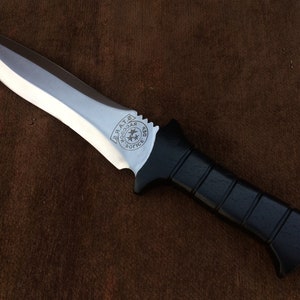 May include: A black-handled knife with a silver blade. The blade has a circular emblem with the words "Woodcar" and "Police Dept." engraved on it.