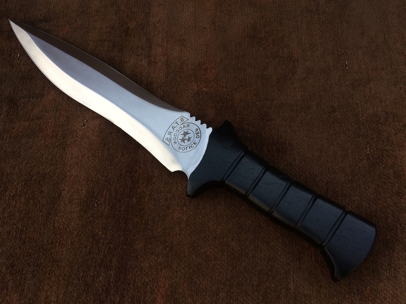 May include: A black-handled knife with a silver blade. The blade has a circular emblem with the words "Woodcar" and "Police Dept." engraved on it.