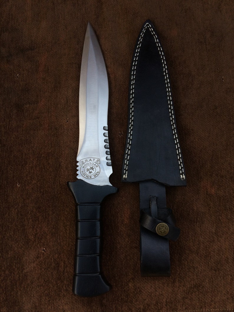 May include: A black-handled knife with a silver blade and a serrated edge. The blade has a circular emblem with the text "S.R.A.T.E.  KOO33AЯ  POLICE DES" on it. The knife is in a black leather sheath with a stitched edge.