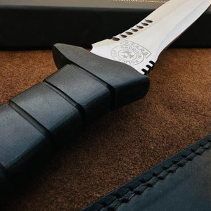 May include: A black tactical knife with a serrated blade and a black rubber handle. The blade has the words "S.T.A.R.S. Raccoon Police Dep." engraved on it.