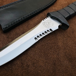 May include: A silver knife with a black handle and a serrated edge. The knife has a black leather sheath and a logo that reads "STARS Raccoon City Police Dep."