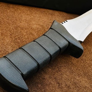 May include: A black and silver knife with a textured black handle. The knife has a sharp blade and a pointed tip.