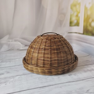 May include: A brown wicker dome-shaped basket with a metal handle. The basket is sitting on a white wooden surface.