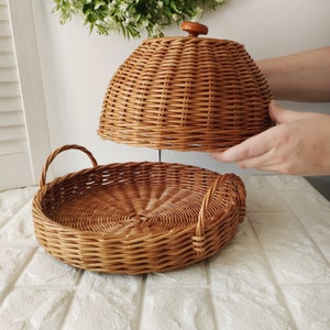 May include: A round wicker serving tray with a dome lid. The tray has two handles and the lid has a wooden knob.