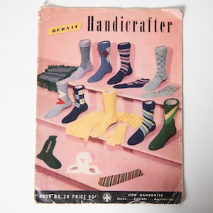 May include: Vintage "Handicrafter" booklet cover featuring various knitted socks in different colors and patterns. The cover is pink with the title in black and yellow. The booklet also features a scarf and gloves.