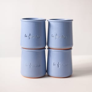 May include: Four blue ceramic cups with the text "la fermiere" embossed on each. The cups are stacked in two pairs.