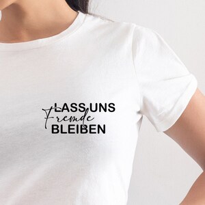Könnte beinhalten: Weißes T-Shirt mit schwarzem Text, der "Lass uns fremde bleiben" lautet.