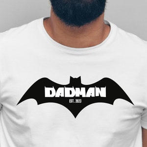 Könnte beinhalten: Weißes T-Shirt mit einem schwarzen Fledermaus-Motiv und dem Text "DADMAN EST. 2023" auf der Vorderseite.