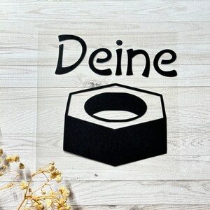 Könnte beinhalten: Ein schwarz-weißer Aufkleber mit dem Wort "Deine" und einer schwarzen sechseckigen Form, die einem Muttern ähnelt.