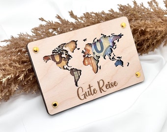 Könnte beinhalten: Ein Holzschild mit einer Weltkarte-Aussparung, die ein Design aus Euro-Scheinen zeigt. Das Schild hat goldfarbene Schrauben und der Text "Gute Reise" ist unten eingraviert.