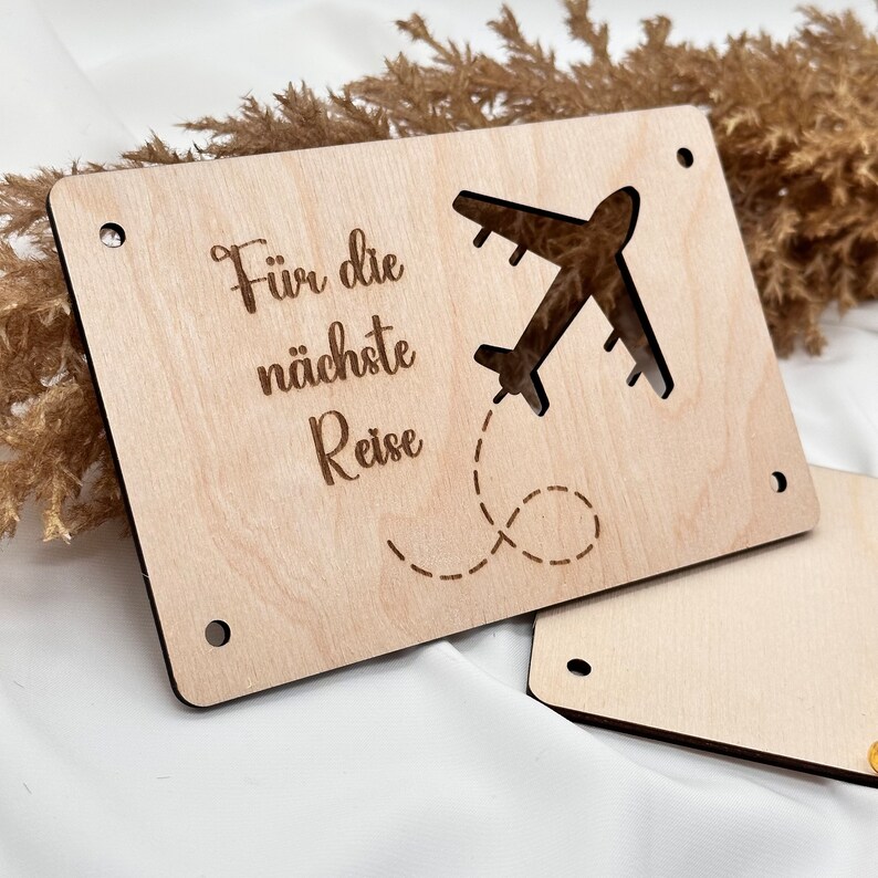 K&ouml;nnte beinhalten: Ein Holzschild mit dem Text "F&uuml;r die n&auml;chste Reise" und einem ausgeschnittenen Flugzeug mit einer gestrichelten Linienspur.