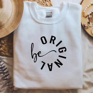 Könnte beinhalten: Weißer Pullover mit schwarzem Text, der in einem Kreis "be original" lautet.