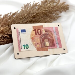K&ouml;nnte beinhalten: Eine Holzplakette mit einem 10-Euro-Schein daran befestigt. Der Schein ist teilweise sichtbar und zeigt den Nennwert und die Flagge der Europ&auml;ischen Union.