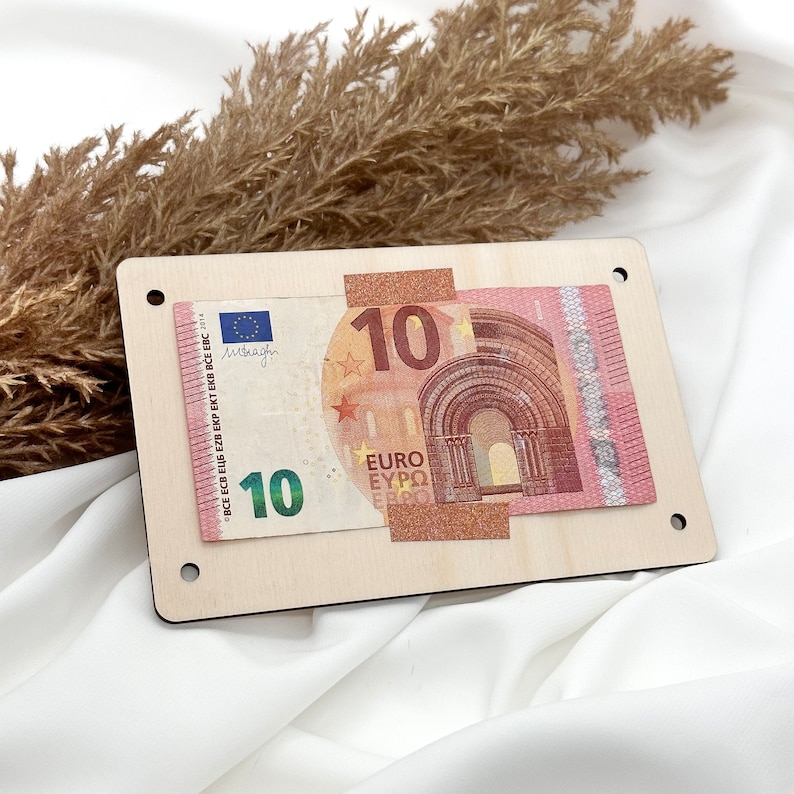 K&ouml;nnte beinhalten: Eine Holzplakette mit einem 10-Euro-Schein daran befestigt. Der Schein ist teilweise sichtbar und zeigt den Nennwert und die Flagge der Europ&auml;ischen Union.