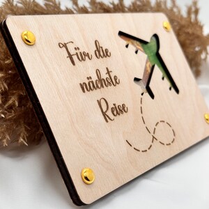 K&ouml;nnte beinhalten: Ein Holzschild mit einem ausgeschnittenen Flugzeugdesign und dem Text "F&uuml;r die n&auml;chste Reise". Das Schild hat goldfarbene Metallakzente.