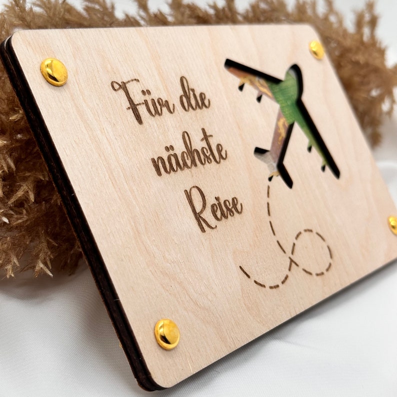 K&ouml;nnte beinhalten: Ein Holzschild mit einem ausgeschnittenen Flugzeugdesign und dem Text "F&uuml;r die n&auml;chste Reise". Das Schild hat goldfarbene Metallakzente.