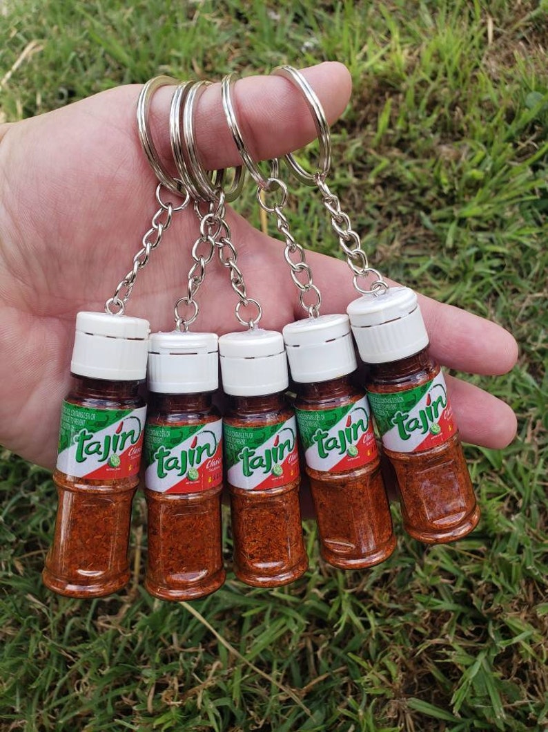 May include: Five miniature glass bottles containing red and orange powder. The bottles are labelled "Tajin" and have a green, white and red label. The bottles are attached to silver keyrings.