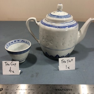 Puede incluir: Una tetera y una taza de té de porcelana blanca con patrones geométricos azules. La tetera tiene tapa y boquilla. La taza de té es pequeña y redonda. El juego está sobre una superficie azul.