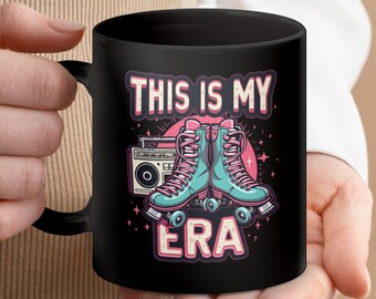 May include: Black coffee mug with a white design featuring a retro boombox, roller skates, and the text "This is my ERA".