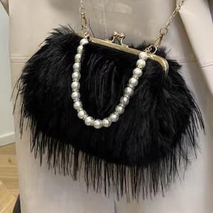 May include: A black faux fur clutch with a gold-tone clasp and chain strap. The clutch features a pearl and rhinestone handle. The bag is rectangular and has a soft, textured appearance.