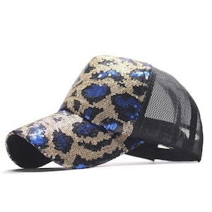 May include: A baseball cap with a leopard print design. The cap features a black mesh back and a front panel covered in gold and blue sequins. The brim is black.