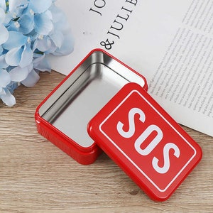 May include: A red rectangular tin with the lid slightly ajar, revealing a shiny interior. The lid features the word "SOS" in white block letters on a red background. The tin is likely for storage.