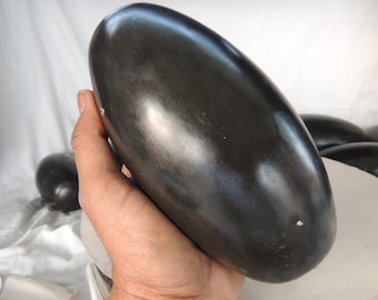 May include: A smooth, black, oval-shaped stone with a glossy finish. The stone is being held in a hand.