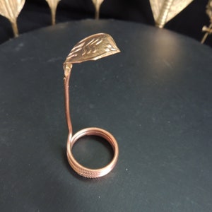 May include: A copper-coloured metal snake-shaped ring holder. The holder is made of wire and has a coiled base. The top of the holder is shaped like a snake's head.