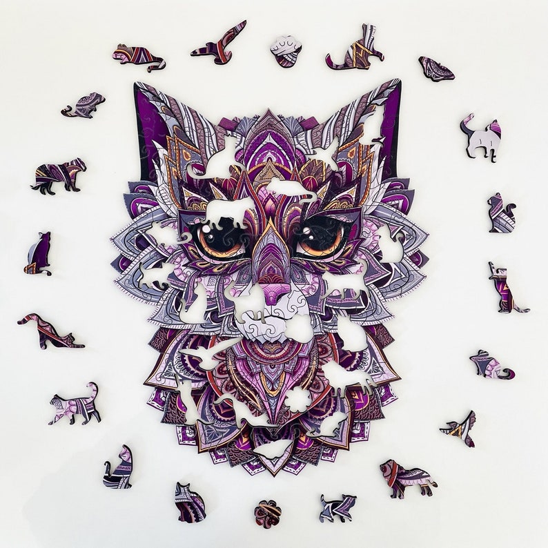 May include: A purple and white intricate cat-shaped jigsaw puzzle with a mandala design. The puzzle pieces are scattered around the cat, which is in the center of the image.