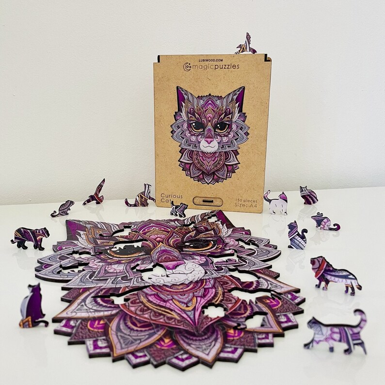 May include: A 150-piece wooden jigsaw puzzle of a curious cat with intricate purple and pink mandala designs. The puzzle is assembled on a white surface with extra pieces scattered around. The box for the puzzle is in the background and features the same cat design.