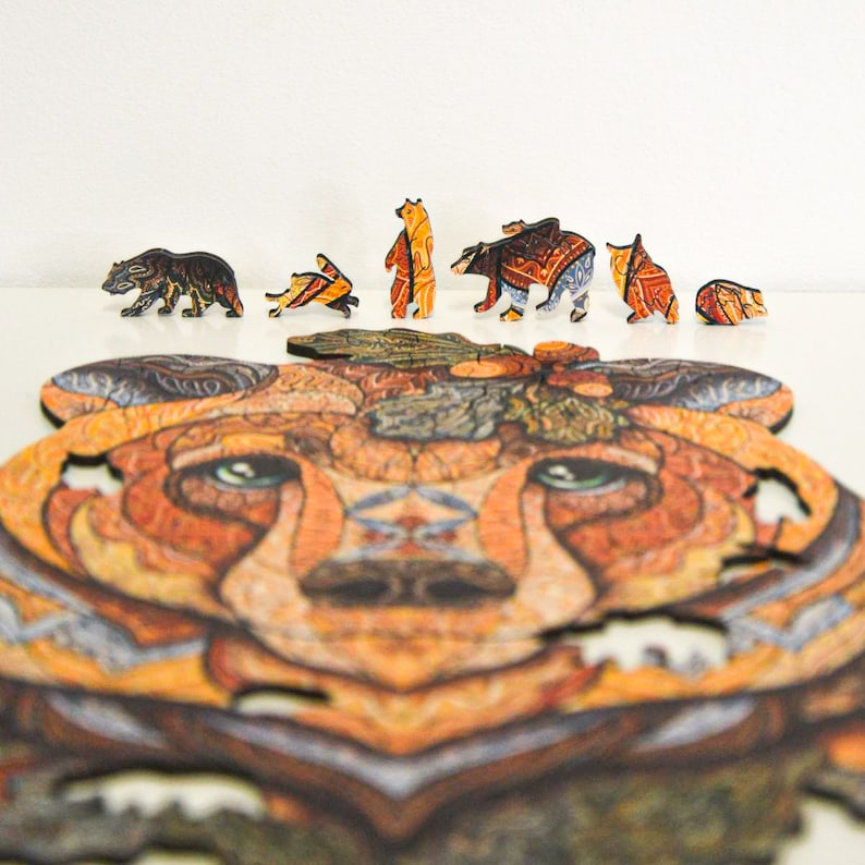 May include: A wooden bear puzzle with several bear-shaped pieces and a large, detailed bear face. The puzzle pieces are various sizes and feature intricate designs in shades of brown, orange, and blue. The completed puzzle is partially assembled.