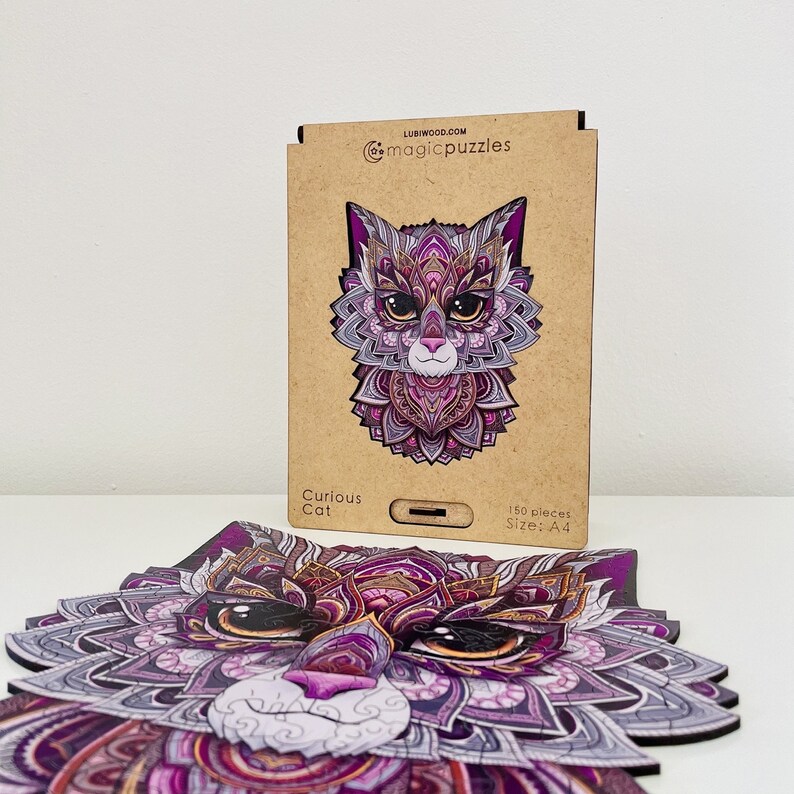 May include: A 150-piece wooden jigsaw puzzle of a purple and pink cat with intricate mandala-like patterns. The puzzle is called "Curious Cat" and is A4 size.