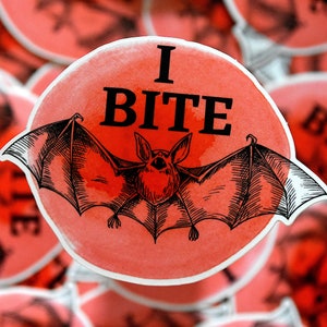 May include: A red circle sticker with a black and white illustration of a bat with the text "I BITE" in black.
