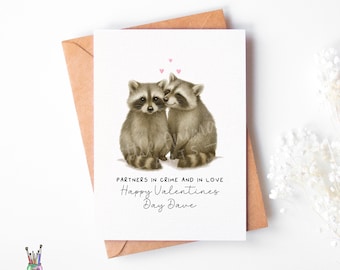 May include: A Valentine's Day card featuring two raccoons, with the text "PARTNERS IN CRIME AND IN LOVE" and "Happy Valentines Day Dave". The card is on a brown envelope, with a small logo in the bottom left corner.