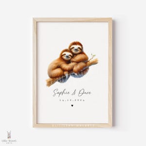 May include: A framed print showing two brown sloths on a branch. The print includes the names "Sophie & Dave" and the date "14.12.2024" in script, with a heart symbol. The artwork is set against a white background, in a light wooden frame.