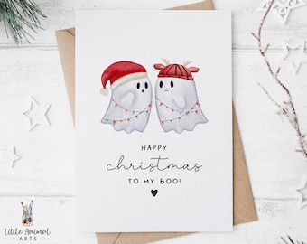 May include: A Christmas card featuring two ghosts wearing Santa hats and reindeer antlers. The ghosts are holding hands and have Christmas lights around them. The card reads "Happy Christmas to my Boo!"