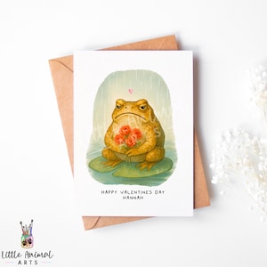 Puede incluir: Tarjeta de San Valentín con una rana gruñona sosteniendo un ramo de rosas rojas. La rana está sentada en una hoja de nenúfar, con un corazón rosa encima. El texto dice "Happy Valentine's Day Hannah".