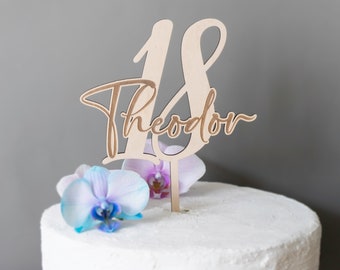 May include: Wooden cake topper with the number 18 and the name Theodor written in cursive. The topper is on a white cake with purple and blue orchids.