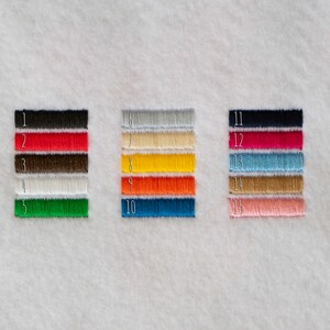 May include: Fifteen embroidered thread samples in a range of colours: black, red, brown, white, green, grey, beige, yellow, orange, blue, navy, fuchsia, turquoise, gold, and pink. Each sample is numbered.