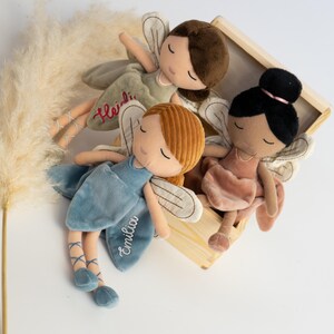 以下が含まれることがあります： 刺繍入りの羽と閉じた目を持つ3体のぬいぐるみ妖精人形。1体は茶色の髪でHeidiという名前入りの緑色のドレス、1体は赤毛でEmiliaという名前入りの青いドレス、もう1体は黒髪でピンクのドレスを着ています。