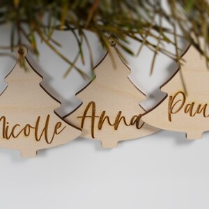 May include: Three wooden Christmas tree ornaments with the names "Nicole", "Anna", and "Paul" engraved on them.